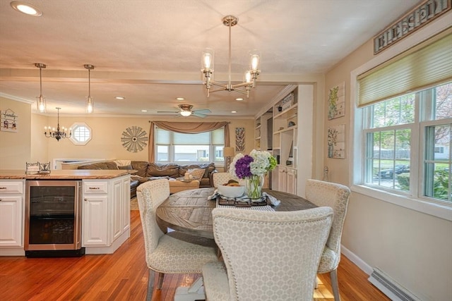 dining area featuring wine cooler, baseboards, baseboard heating, light wood-style flooring, and ceiling fan with notable chandelier