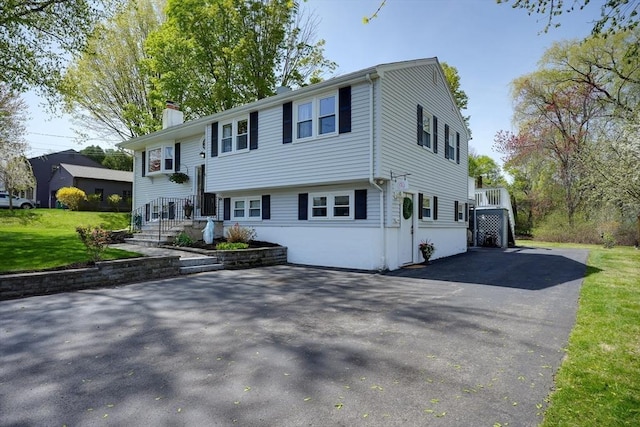 view of front of house featuring driveway, a chimney, and a front lawn