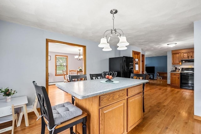 24 Floyd Ave, Tewksbury, MA 01876 - kitchen with black appliances, a chandelier, under cabinet range hood, a breakfast bar, and light wood-type flooring