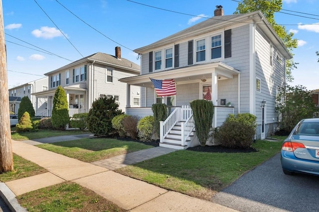 traditional style home with covered porch, a chimney, and a front yard
