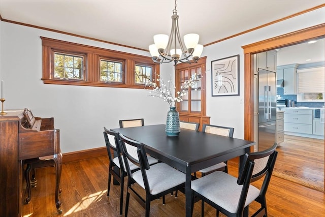 dining space with baseboards, an inviting chandelier, ornamental molding, and light wood-type flooring
