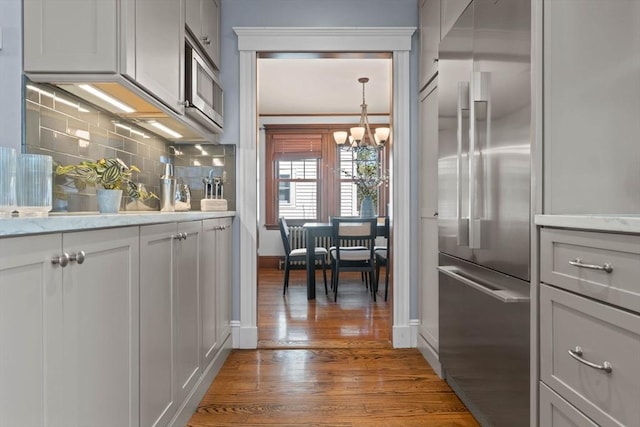 bar featuring a notable chandelier, appliances with stainless steel finishes, baseboards, wood finished floors, and tasteful backsplash