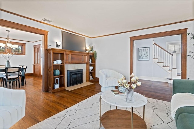 living room featuring crown molding, an inviting chandelier, baseboards, wood finished floors, and visible vents