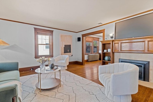 living area with crown molding, radiator, wood finished floors, and a fireplace