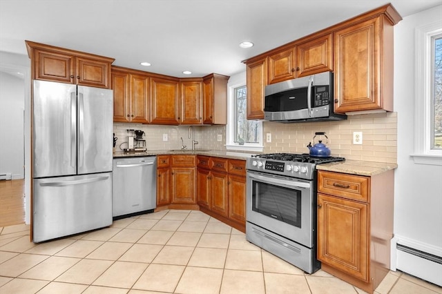 kitchen with a baseboard heating unit, tasteful backsplash, stainless steel appliances, brown cabinetry, and light stone countertops