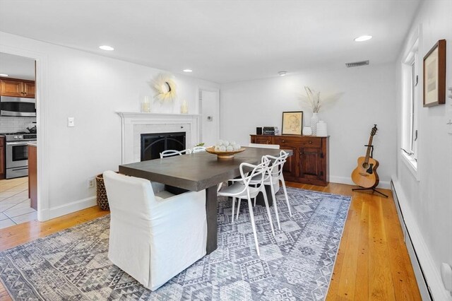 dining room featuring light wood-style flooring, a fireplace, a baseboard heating unit, and baseboards