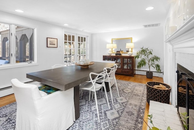 dining room with visible vents, wood finished floors, a healthy amount of sunlight, and a glass covered fireplace