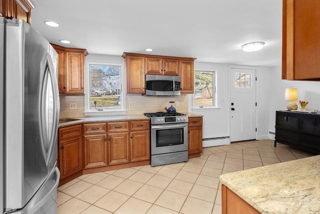 kitchen with tasteful backsplash, a baseboard heating unit, brown cabinets, appliances with stainless steel finishes, and light tile patterned flooring