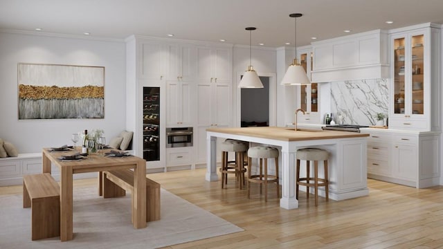 kitchen featuring an island with sink, decorative light fixtures, white cabinetry, and stainless steel oven