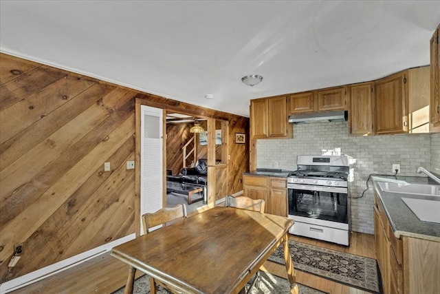 kitchen featuring sink, light wood-type flooring, wooden walls, and stainless steel range with gas stovetop