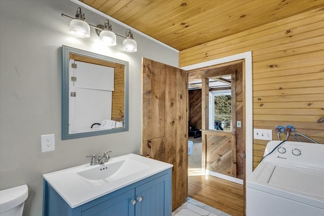 bathroom featuring washer / dryer, vanity, toilet, and wood walls