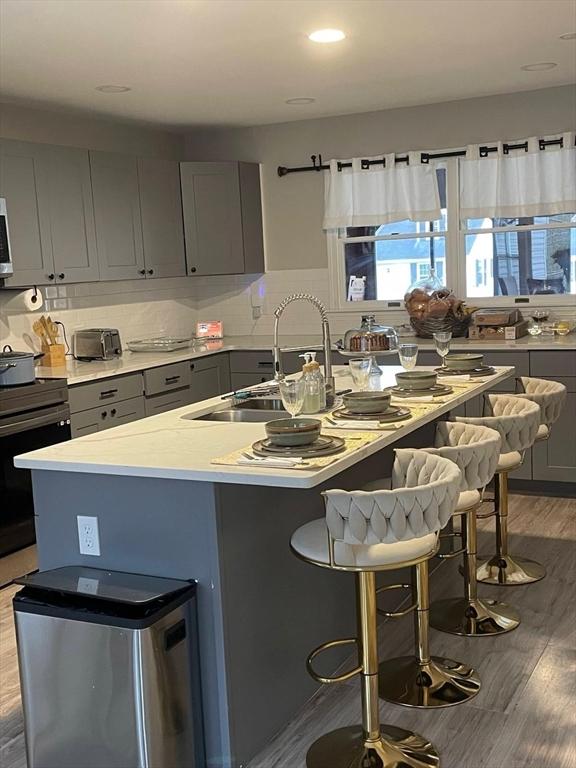 kitchen with a breakfast bar area, gray cabinetry, wood-type flooring, a center island with sink, and appliances with stainless steel finishes