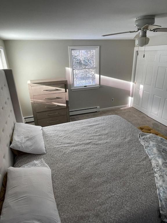 unfurnished bedroom with multiple windows, ceiling fan, and baseboard heating