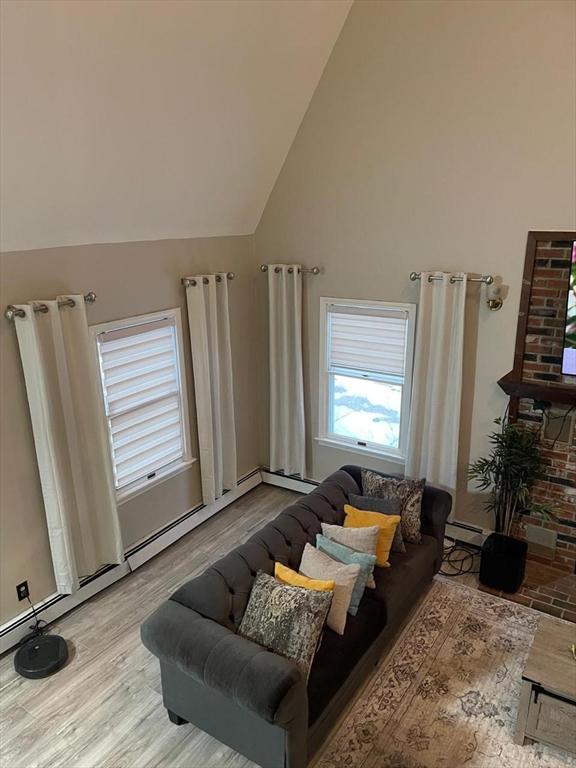 living room featuring a baseboard radiator, high vaulted ceiling, and light hardwood / wood-style flooring