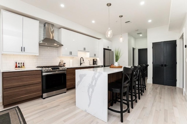 kitchen with appliances with stainless steel finishes, light countertops, wall chimney range hood, white cabinetry, and backsplash