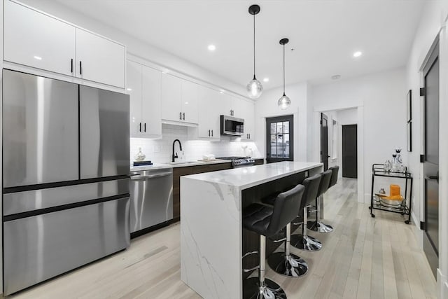 kitchen featuring white cabinets, decorative backsplash, a kitchen island, stainless steel appliances, and a sink