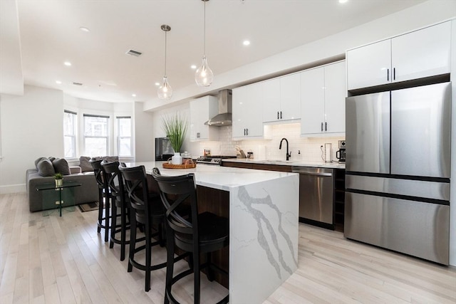 kitchen with stainless steel appliances, decorative backsplash, a sink, wall chimney range hood, and a kitchen island