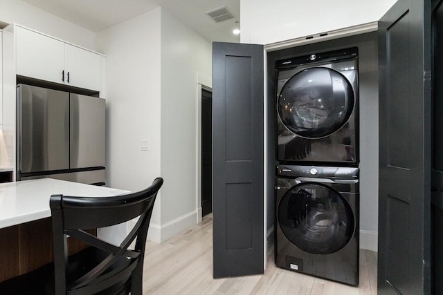 laundry room with visible vents, light wood-style flooring, stacked washer / dryer, laundry area, and baseboards