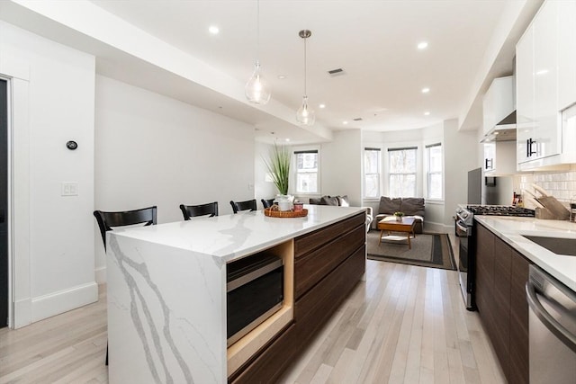 kitchen with tasteful backsplash, white cabinets, modern cabinets, appliances with stainless steel finishes, and light wood-style floors