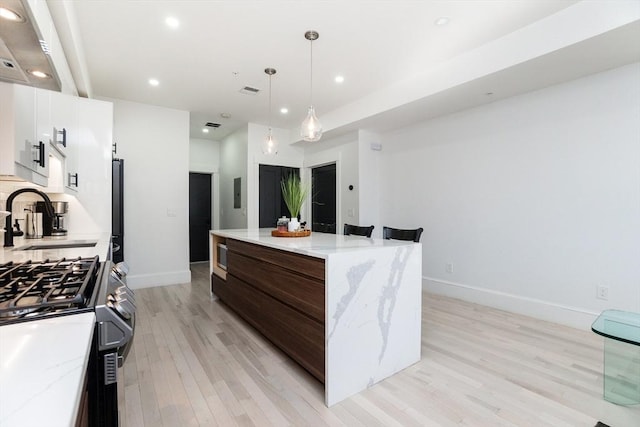 kitchen with recessed lighting, light wood-style floors, white cabinetry, a kitchen island, and a sink