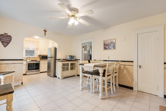 kitchen with ceiling fan, appliances with stainless steel finishes, light tile patterned floors, and tile walls