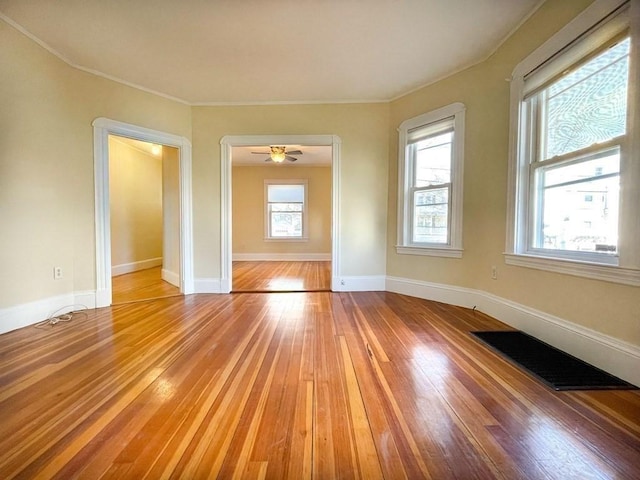 empty room featuring light wood finished floors, baseboards, visible vents, ceiling fan, and ornamental molding