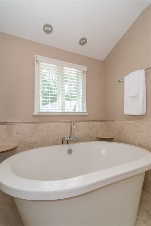 bathroom featuring tile patterned flooring, a bath, and vaulted ceiling