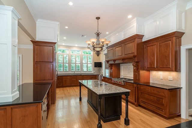 kitchen featuring a center island with sink, crown molding, light wood-type flooring, stainless steel gas cooktop, and a chandelier