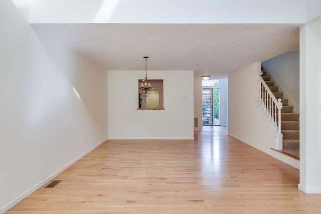 spare room with an inviting chandelier, floor to ceiling windows, and light wood-type flooring