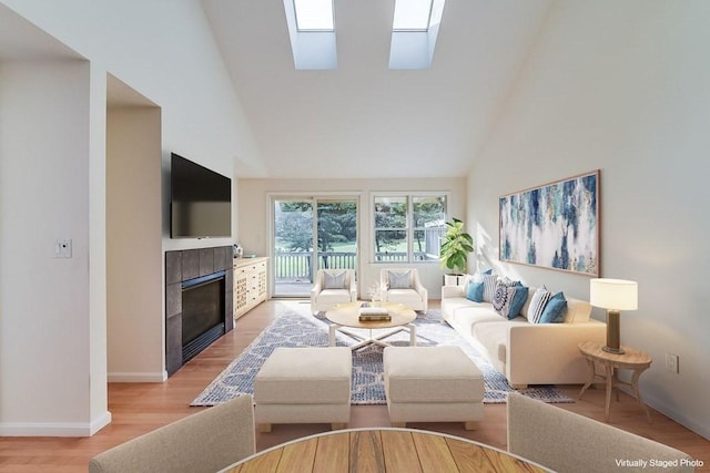 living room with a skylight, a high ceiling, a tile fireplace, and light hardwood / wood-style flooring