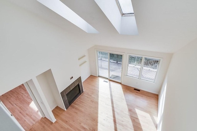 unfurnished living room with a tile fireplace, lofted ceiling with skylight, a wealth of natural light, and light hardwood / wood-style floors