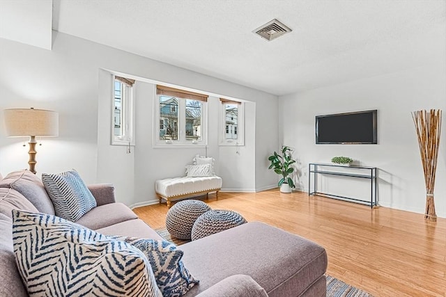 living room featuring a textured ceiling, light wood finished floors, visible vents, and baseboards