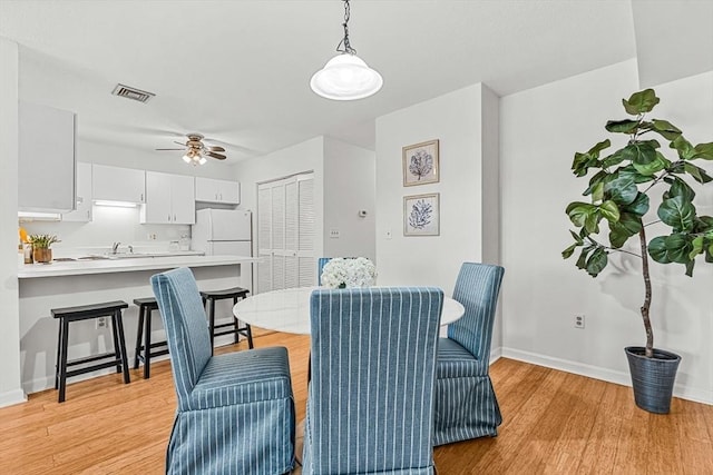 dining room with light wood finished floors, baseboards, visible vents, and a ceiling fan