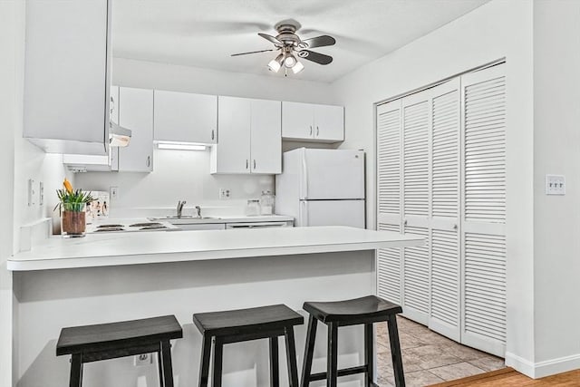 kitchen featuring a ceiling fan, freestanding refrigerator, a peninsula, light countertops, and a kitchen bar