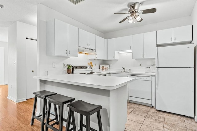 kitchen with a breakfast bar area, under cabinet range hood, a peninsula, white appliances, and light countertops