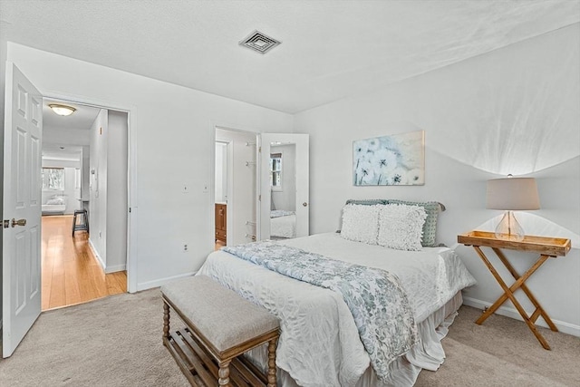 carpeted bedroom with visible vents, connected bathroom, and baseboards