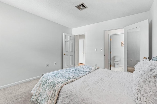 bedroom with a textured ceiling, ensuite bathroom, carpet floors, visible vents, and baseboards