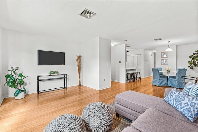 living area with baseboards, visible vents, and light wood-style floors