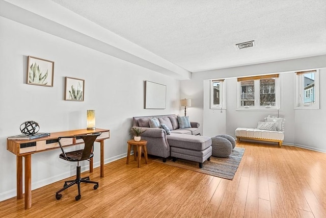 interior space featuring light wood-style floors, visible vents, a textured ceiling, and baseboards