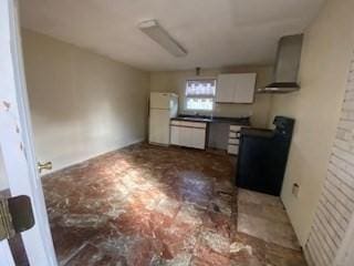 kitchen featuring stove, wall chimney exhaust hood, white cabinets, and freestanding refrigerator