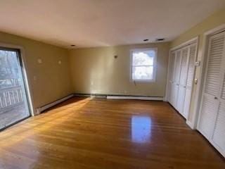 unfurnished bedroom featuring a baseboard heating unit, two closets, and wood finished floors