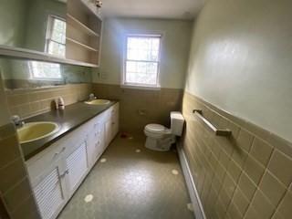 bathroom featuring double vanity, toilet, a wainscoted wall, and a sink