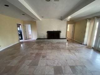 unfurnished living room featuring beamed ceiling, a fireplace with raised hearth, and baseboards