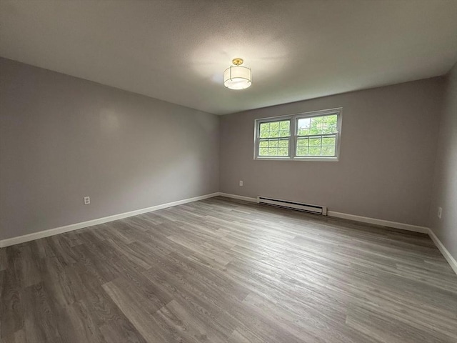unfurnished room featuring wood finished floors, baseboards, and a baseboard heating unit