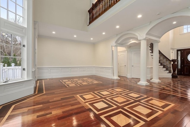 unfurnished room featuring dark hardwood / wood-style floors, a towering ceiling, ornamental molding, and ornate columns