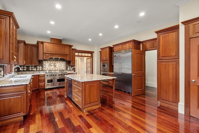 kitchen featuring light stone countertops, dark hardwood / wood-style flooring, a kitchen island with sink, sink, and built in appliances