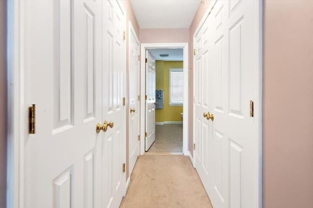 corridor featuring baseboards and light colored carpet