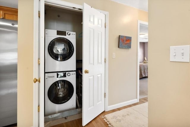 laundry room with baseboards, laundry area, stacked washer / dryer, and wood finished floors