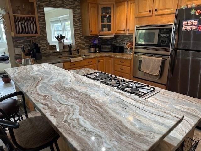 kitchen featuring appliances with stainless steel finishes, sink, a kitchen bar, decorative backsplash, and light stone counters