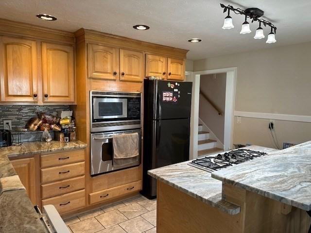 kitchen featuring light stone counters, appliances with stainless steel finishes, light tile patterned flooring, and decorative backsplash